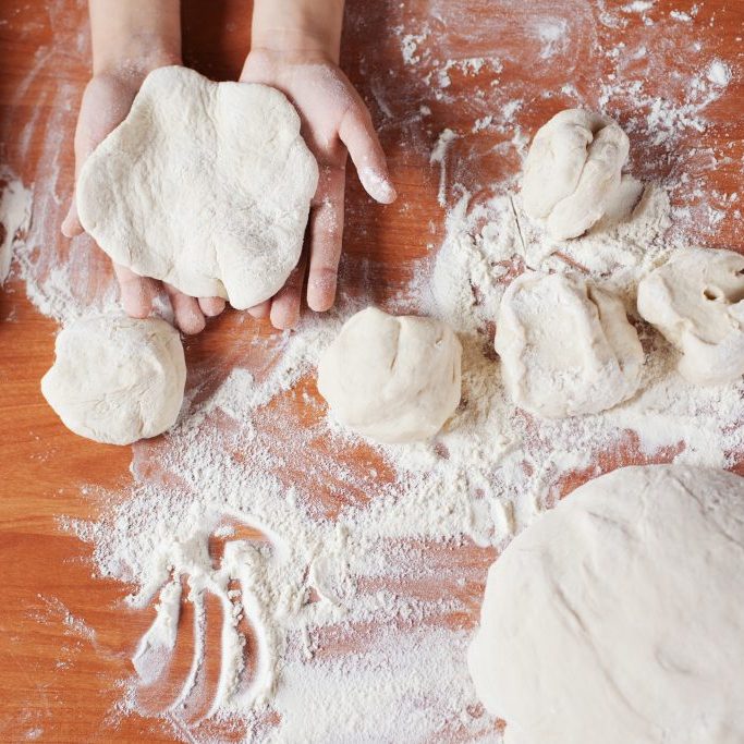 Child holding kneading dough. Kid's hands and fresh dough, flour and rolling-pin on table. Cooking pies at home or  learning at culinary class.